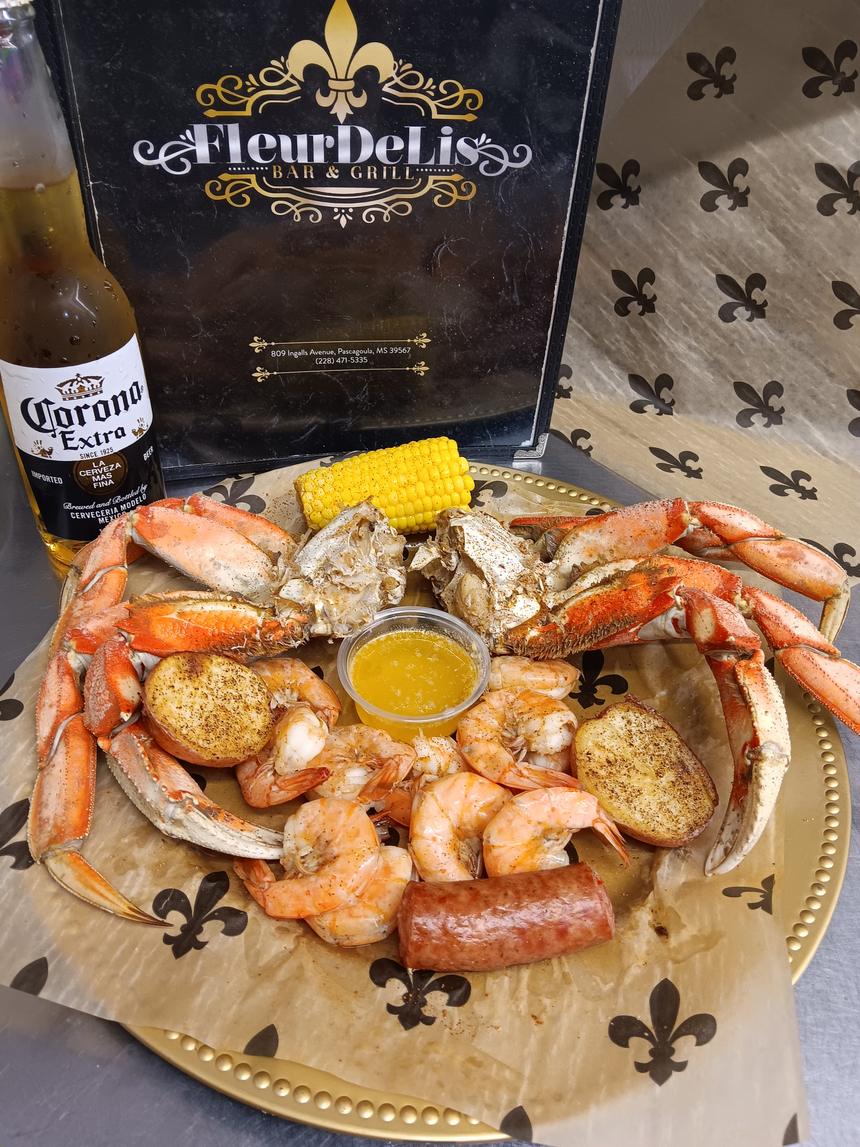 A Fleur De Lis seafood boil platter of crab, shrimp, sausage and corn on a fleur-de-lis printed liner, next to the Fleur De Lis menu